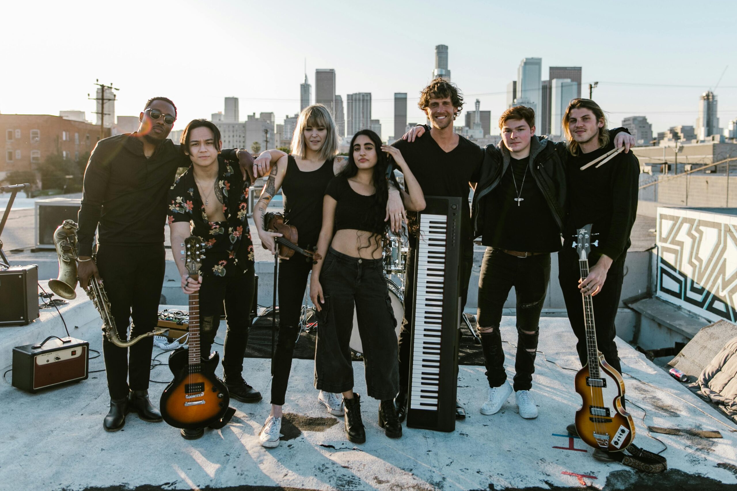 A diverse group of musicians posing on a rooftop with a city skyline in the background.